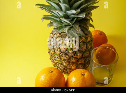 Ananas singolo isolato su sfondo giallo con vetro vuoto e mandarini arance collocato in mezzo tondo. Foto Stock
