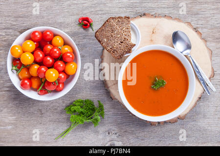 Zuppa di pomodoro con erbe frresh, peperoncino, pomodoro e la crema sul buio tavolo in legno Foto Stock