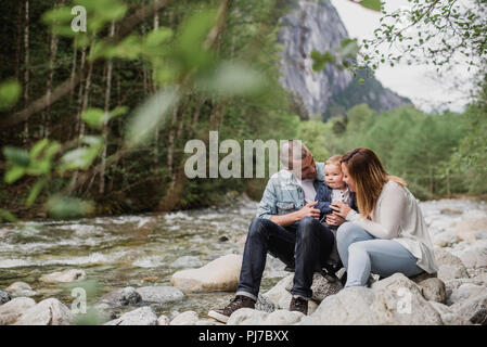 I genitori e il bambino figlio seduti sulle rocce lungo il torrente Foto Stock