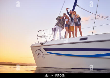 Amici con smart phone tenendo selfie sul catamarano al tramonto Foto Stock