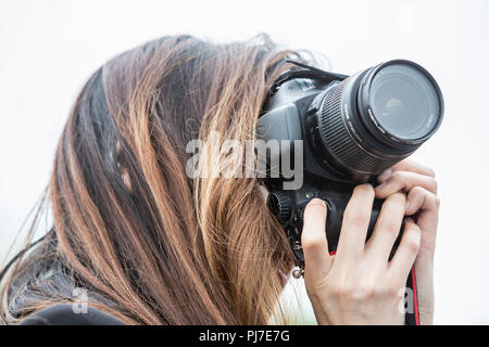 Una giovane donna in possesso di una fotocamera digitale SLR scatta una fotografia, i suoi lunghi capelli ha caduto oltre il suo viso si nascondono e rendendo il suo unidnetifiable. Foto Stock