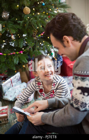 Padre libro di lettura con la figlia ad albero di Natale Foto Stock