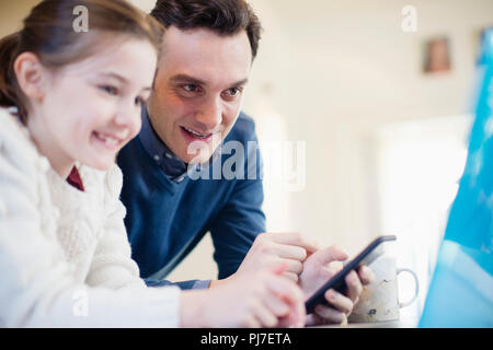 Padre con smart phone utilizzando computer portatile con la figlia Foto Stock