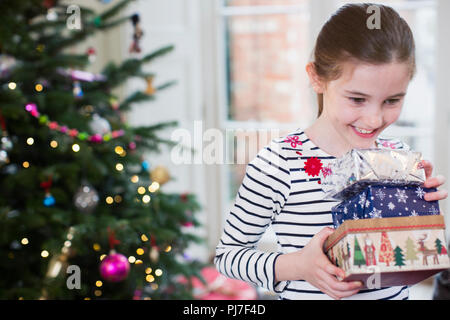 Sorridente, desiderosa ragazza raccogliendo i regali di Natale in salotto Foto Stock