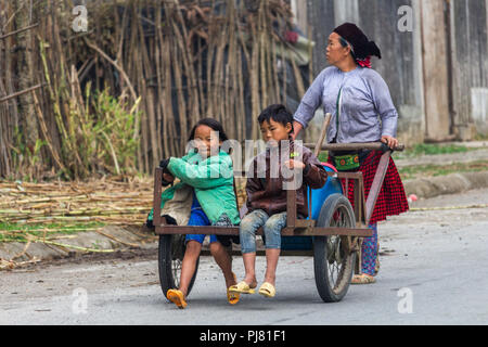 Ha Giang, Vietnam - Marzo 18, 2018: Madre portante due bambini su un carrello manuale in una remota zona rurale del nord del Vietnam Foto Stock