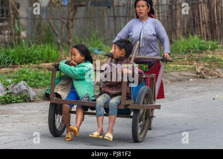 Ha Giang, Vietnam - Marzo 18, 2018: Madre portante due bambini su un carrello manuale in una remota zona rurale del nord del Vietnam Foto Stock