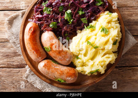 Servite la purea di patate in umido con cavolo rosso e salsicce fritte close-up su una piastra su un tavolo. Parte superiore orizzontale vista da sopra Foto Stock