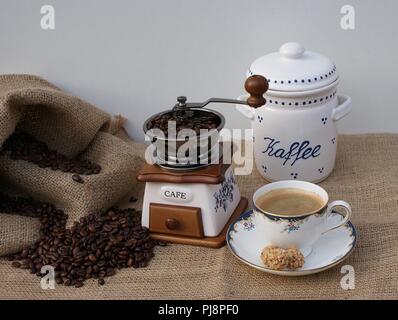 Chiudere con il macinino da caffè, una tazza di caffè, caffè in porcellana, stagno sacco di caffè con caffè in grani Foto Stock