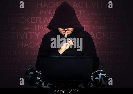 L'uomo con la faccia nascosta lavorando a un computer. Tenendo un dito per la sua bocca. Hacker di rubare i dati da un computer portatile concetto per la protezione della rete, ho Foto Stock