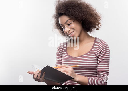 Clever dai capelli scuri studente ricci facendo il suo dovere fare alcune note Foto Stock