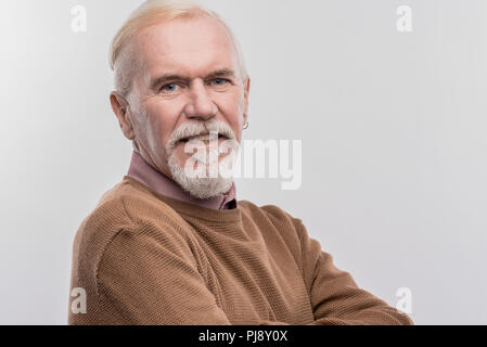 Anziani blue-eyed uomo che indossa il marrone scuro maglione sorridente largamente Foto Stock