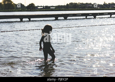 Poco ragazza camminare in acqua poco profonda nel tramonto Foto Stock