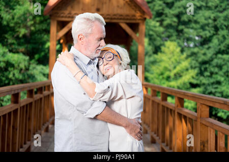 Sorridente raggiante signora anziana appoggiata al suo uomo bello Foto Stock