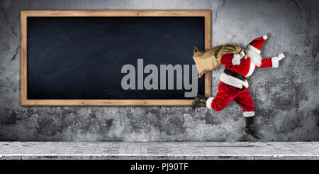 Santa Claus in fretta con il sacco pieno di regali in esecuzione jumping astratta Natale divertente xmas calcestruzzo affissioni lavagna vuota sfondo con cop Foto Stock