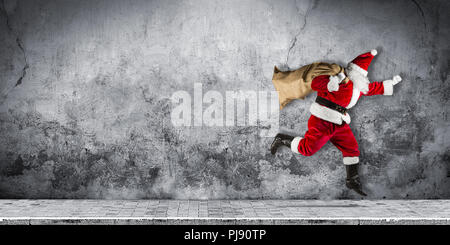 Fine santa claus in fretta con tradizionale rosso bianco costume e una borsa piena di regali in esecuzione jumping astratta Natale divertente xmas backgro concrete Foto Stock
