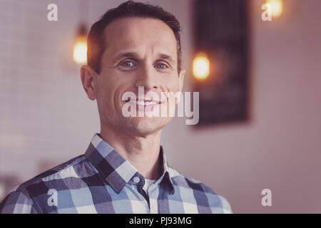 Bello fiducioso uomo sorridente essendo nella luminosa sala. Foto Stock