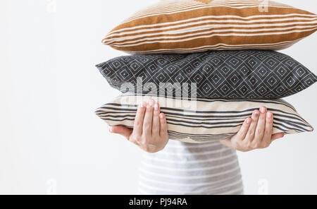 Le mani della donna moderna azienda tre cuscini per divani, muro bianco sfondo nella tendenza, minimalismo pulito accogliente casa concetto. Decorazioni in autunno per vivere la casa Foto Stock