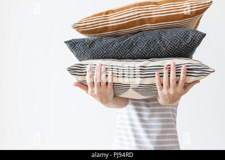 Le mani della donna moderna azienda tre cuscini per divani, muro bianco sfondo nella tendenza, minimalismo pulito accogliente casa concetto. Decorazioni in autunno per vivere la casa Foto Stock