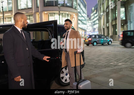 Apertura del driver della porta auto per l uomo d affari con la valigia sulla strada urbana di notte Foto Stock