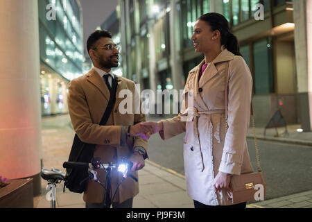 La gente di affari con le procedure di handshaking per bicicletta sul marciapiede urbano di notte Foto Stock