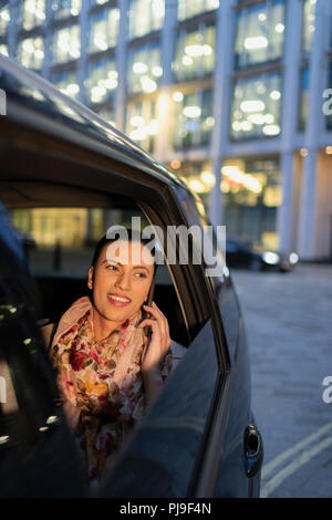 Sorridente imprenditrice parlando su smart phone in crowdsourced taxi di notte Foto Stock
