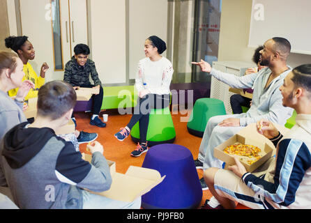 Gli adolescenti e mentore di parlare e mangiare la pizza in centro nella comunità Foto Stock