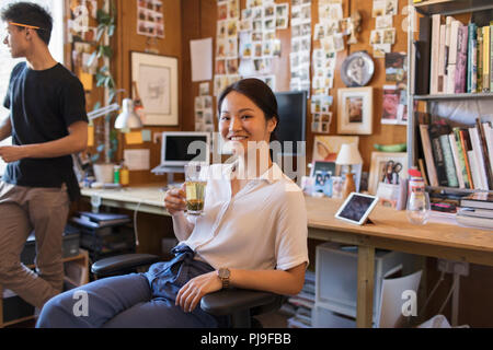 Ritratto sorridente e fiducioso imprenditrice creativa bere il tè in ufficio Foto Stock