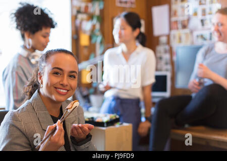 Ritratto sorridente e fiducioso imprenditrice creativa di mangiare sushi in ufficio Foto Stock