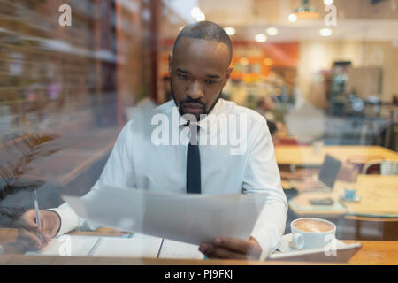 Imprenditore focalizzato la revisione di documenti cartacei, lavorando nella finestra cafe Foto Stock