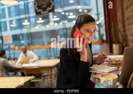 Sorridente imprenditrice parlando su smart phone e lavorare al computer portatile in cafe Foto Stock
