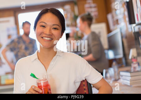 Ritratto sorridente imprenditrice creativa di bere succo di frutta in office Foto Stock