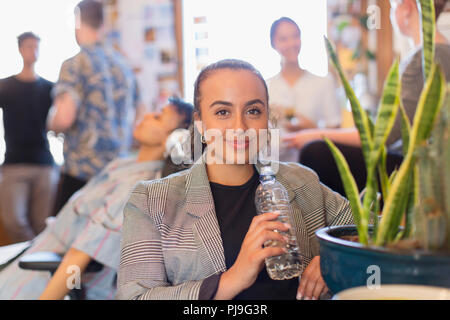 Ritratto fiducioso imprenditrice di bere acqua in bottiglia in ufficio Foto Stock