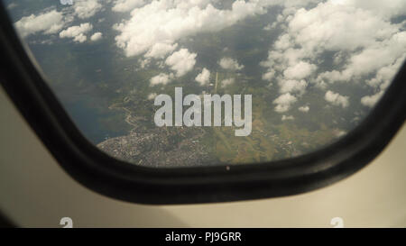 Vista attraverso un aereo finestra sull'isola tropicale, oceano mare, cielo e nubi. Vista aerea del mare, le nuvole e il cielo come visto attraverso la finestra di un aeromobile. Concetto di viaggio. Foto Stock