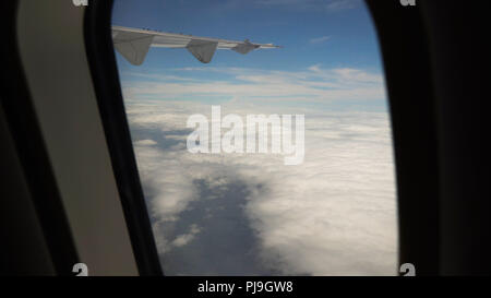 Vista attraverso un aereo finestra sull'isola tropicale, oceano e Cielo e nubi. Vista aerea del mare, le nuvole e il cielo come visto attraverso la finestra di un aeromobile. Concetto di viaggio. Foto Stock