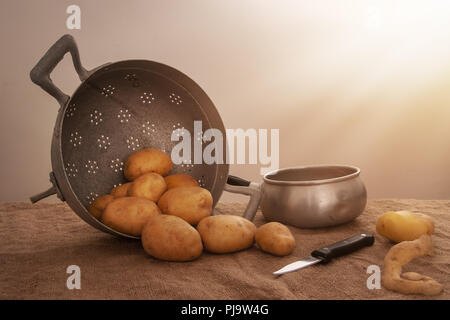 Preparazione alimentare, Pelate le patate in una casa colonica rustica impostazione di vita ancora con la pentola, collander, coltello, hessian aka iuta. Foto Stock