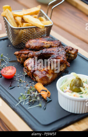 Deliziosi barbecue ali di pollo servito con insalata Coleslaw e patatine fritte sul bordo di taglio Foto Stock