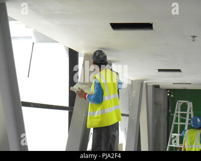 Sito in costruzione i lavoratori stanno facendo intradosso soffitto foglietta lavoro presso il sito di costruzione. Base e finale dello strato di rivestimento di applicare per ottenere la superficie liscia. Foto Stock