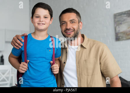 Ritratto di sorridere padre e figlio con zaino in casa, torna al concetto di scuola Foto Stock