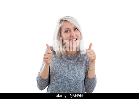 Ritratto di una allegra donna bionda che mostra Thumbs up. Ragazza in abiti casual guardando la telecamera con gioiosa e affascinante sorriso. Spazio di copia, retro bianco Foto Stock