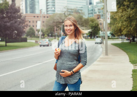 Felice gravidanza sana. Ritratto di gravidanza caucasica bionda e giovane donna caucasica camminando nella trafficata città urbana all'esterno. Bella slim si aspettano sportivo Foto Stock