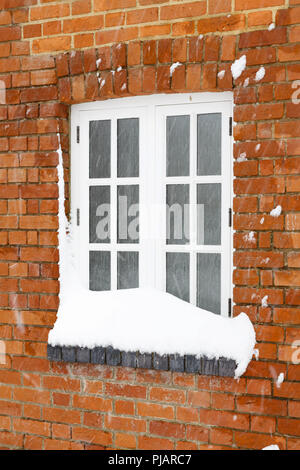 Neve in inverno copre la finestra di una vecchia casa di mattoni in Inghilterra Foto Stock