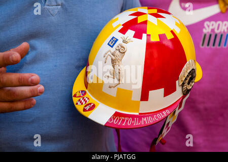 Un uomo dal Valdimontone (RAM) Contrada detiene il casco indossato dalla Contrada Jockey durante il Palio, il Palio di Siena, Siena, Italia Foto Stock