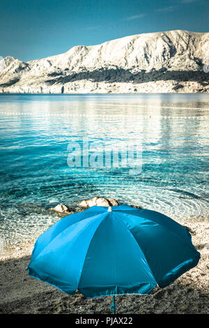 Un lone ombrellone in spiaggia allo spuntar del giorno a bordo delle acque del mar Adriatico a Baska sull'isola di Krk Foto Stock