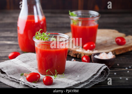 Il succo di pomodoro in vetro con il crescione insalata di pomodori freschi sul tagliere di legno grigio e asciugamano. Foto Stock