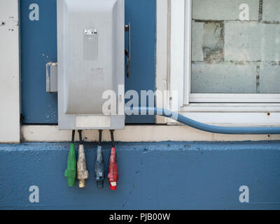 Rosso, bianco, blu e rossa potenza industriale i cavi appesi al di fuori di una scatola dei fusibili Foto Stock