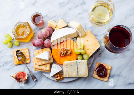 Assortimento di formaggi, uve con il vino bianco e rosso in bicchieri. Sfondo marmo. Vista dall'alto. Foto Stock