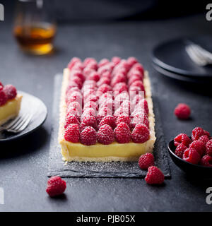 Lampone crostata con crema alla vaniglia e cioccolato bianco sulla scheda di ardesia. Pietra nera dello sfondo. Foto Stock