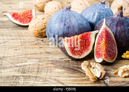 Fichi freschi interi e tagliati con gherigli di noce su una tavola di legno vecchio sfondo Foto Stock