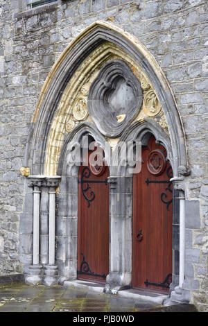 Visualizzazione verticale ad arco di dual gate con porte in legno su cerniere in metallo sulla parete laterale della pietra chiesa medievale. Foto Stock