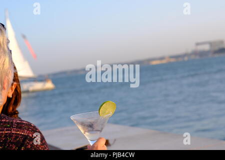 Cocktail in vetro con una fetta di limone contro il fondale del fiume Tolgus a Lisbona Foto Stock